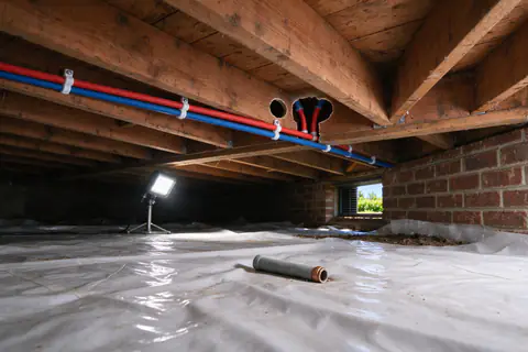 New PEX supply lines running along floor joists in a Charlotte crawl space, with old gray pipe cut out below